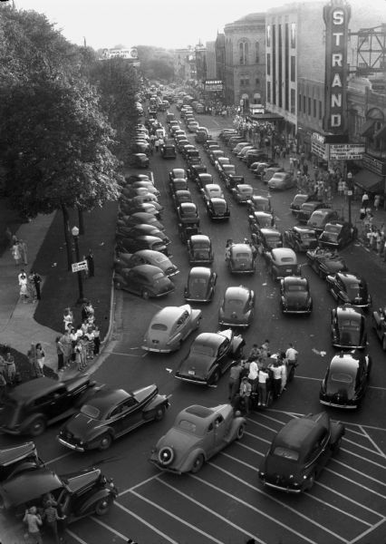 Elevated view of a mass of cars turning from North Pinckney Street onto East Mifflin Street on the Capitol Square celebrating V-J Day, August 15, the day on which the Allies announced the surrender of Japanese forces during World War II. The car loaded with youngsters in the lower part of the picture was the first to circle the square in the course of the hours-long spontaneous celebration.