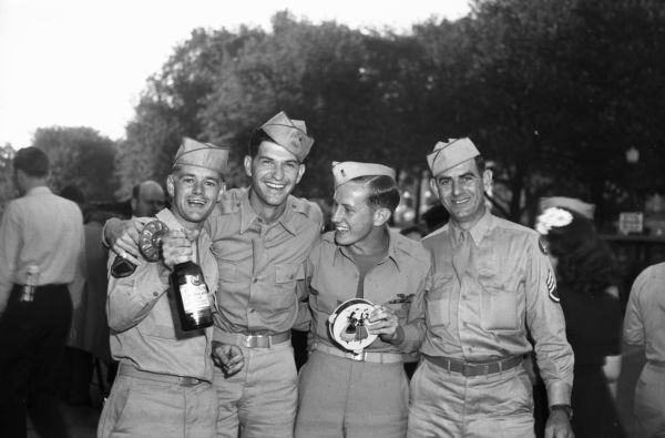 Four soldiers, one with liquor bottle and two others with noisemakers, standing on the Capitol Square. They are celebrating V-J Day, August 15, the day on which the Allies announced the surrender of Japanese forces during World War II.
