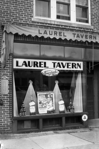 Exterior view of the Laurel Tavern, 2505 Monroe Street. The storefront window contains a display of two Schlitz Beer bottle pyramids, two large bottles of Kinsey Whiskey, and a Fauerbach Beer sign.