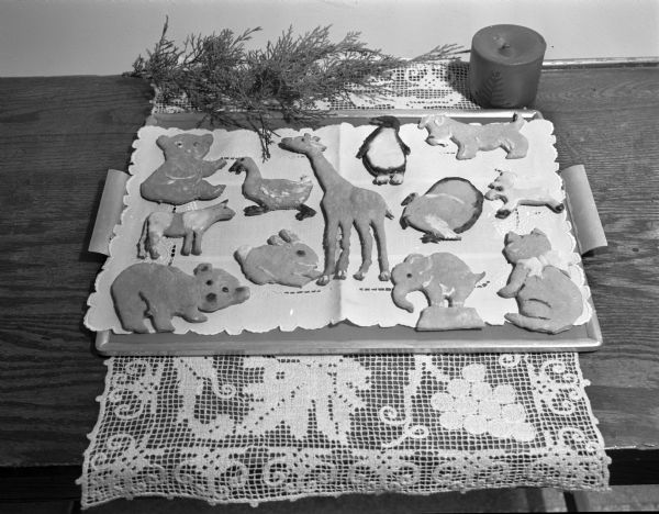 Display of animal cut-out cookies on a tray with a candle and pine boughs.