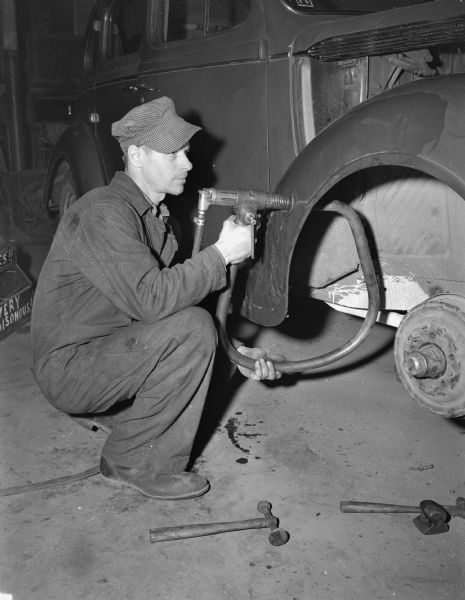 An employee of the Royal Body Company, 9-13 North Brooks Street, operating an air hammer to straighten a dented fender of a automobile.