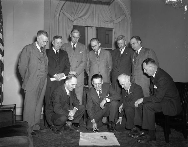 Members of the Madison City Plan Commission examining a proposed new zoning ordinance. Standing, from left, are J.M. Albers of the state planning board, an advisor; City Engineer, T.F. Harrington; Paul E. Stark, advisor; Mayor, F. Halsey Kraege; and Commissioners Roger Kirchoff and Walter Plaenert. Kneeling, from left, are City Attorney, Harold H. Hanson; Building Commissioner, Gordon E. Nelson; Commissioner Henry C. Wolf, president of the city park commission; and Commissioner Robert J. Sutherland.