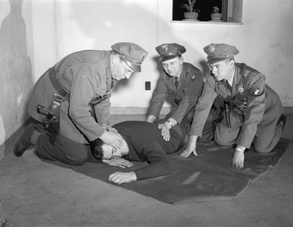 Dane County traffic police receiving first aid training. Officer Rodney Burgenske is performing artificial respiration on Lieut. A.C. Pope while Capt. O.F. Larson frees his face for proper breathing. Officer Ralph Conklin is looking on.