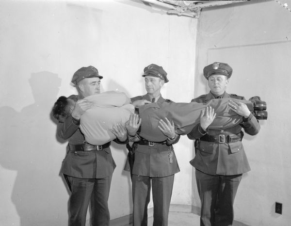 Dane County traffic police receiving first aid training. They are demonstrating the correct way for carrying a victim. From left are Lieut. A.C. Pope, and Officers Ray Case and E.W. Kelzenberg. The victim is fellow Officer Ralph Conklin.