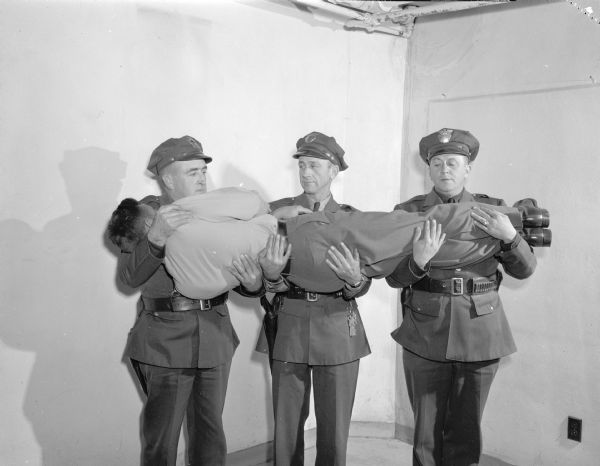 Dane County traffic police receiving first aid training.  They are  demonstrating the correct way for carrying a victim. From left are Lieut. A.C. Pope, and Officers Ray Case and E.W. Kelzenberg.  The victim is fellow Officer Ralph Conklin.