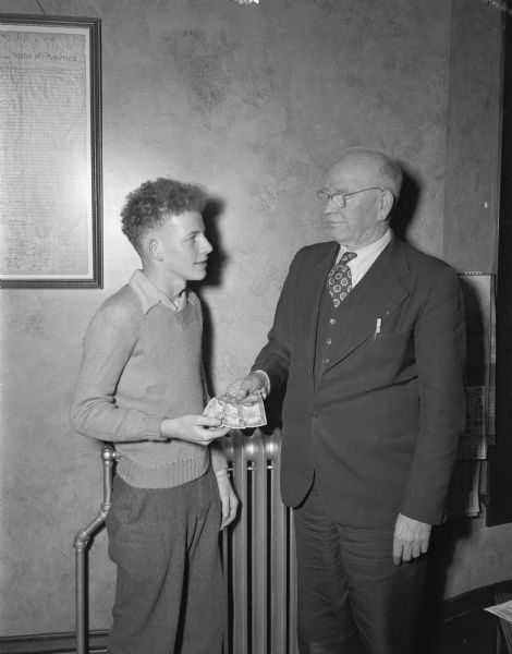 Police Chief William H. McCormick is shown giving eighty dollars to Kenneth Jevens, 14 year old son of Mr. and Mrs. Leonard Jevens, 2318 Sommers Avenue. The youth found eighty dollars on the sidewalk and gave it to the police.  Since there were no claimants, it was returned to Jevems as "honesty is the best policy" example.