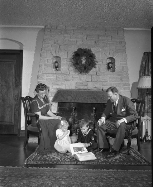 Dana (?) family. Mother, father, son, and daughter, in front of home fireplace.