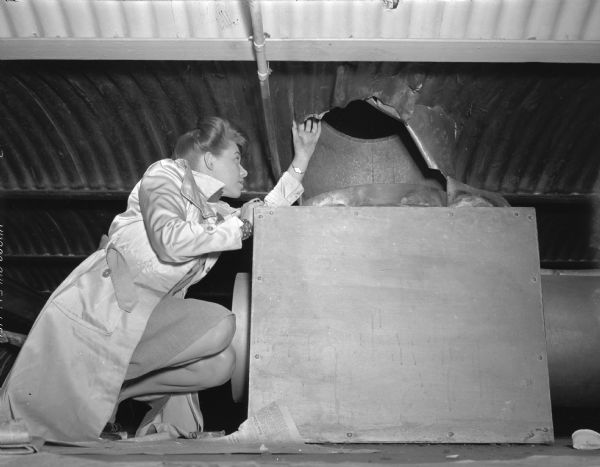 June Dieckman, police reporter for the "Wisconsin State Journal," shown examining a hole in a ventilating pipe cut by two federal prisoners attempting to escape, after having pried their cell door open.
