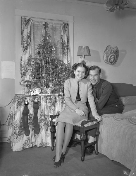 An unidentified couple (Pilscher?) seated in a bedroom.  Behind them is a small Christmas tree and two Christmas stockings.
