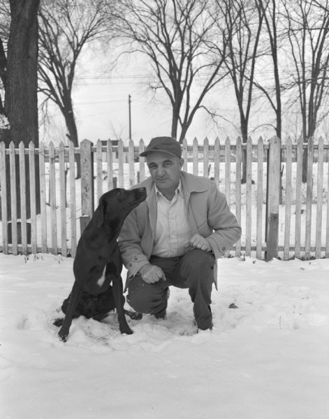 Nick Bonerich (?) and a dog outside in the snow, with a yard, fence, and trees in the background.