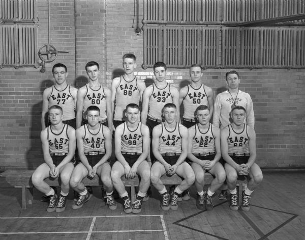 Group portrait of Madison East High School basketball team in uniform with the coach.