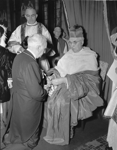 Leo Crowley kneeling before the Most Rev. Moses E. Kiley, Archbishop of Milwaukee Archdiocese, during a mass in St. Mary's Hospital Chapel of Our Lady of Good Counsel. Crowley was bestowed with the title of Knight Commander with the Star of the Order of Pius IX.