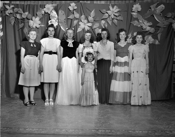 Group portrait of seven females and one young girl in formals and street dresses from the Emporium Department Store that they modeled in the Cottage Grove Graded School style show.  The two women on the left are Eleanor Arndt and Rosemary Coyle, 10th graders.  The woman second from the right is the young girl's mother.