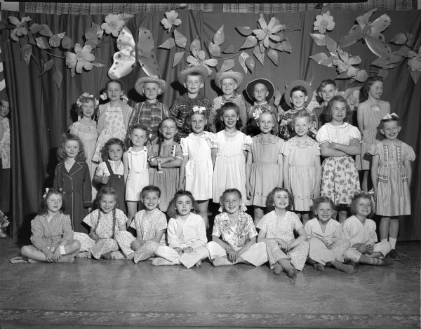 Group portrait of 27 children in the Cottage Grove Grade School Style Show, modeling clothes from the Emporium Department Store. Front row left to right: Carol Miller, Diane Duckert, Peggy Coffey, Dorothy Thorstad, Janice Gullickson, Cecelia Fredenberg, Janice Clawson, and Barbara Schultz. Second row left to right: Judy Wick, Katherine Thornton, Patty Thornton, Delma Hammond, Jean Ann Blackman, Betty Hauge, Florence Maly, Yvonne Carpenter, Patty Vincent, and Betty Payne. Back row left to right: Jeanne Hestness, Diane Kelly, Darrell Thompson, Bob Witte, Duane Hestness, Douglas Duckert, Bobby Hauge, Don Thorstand, and Betty Renz.