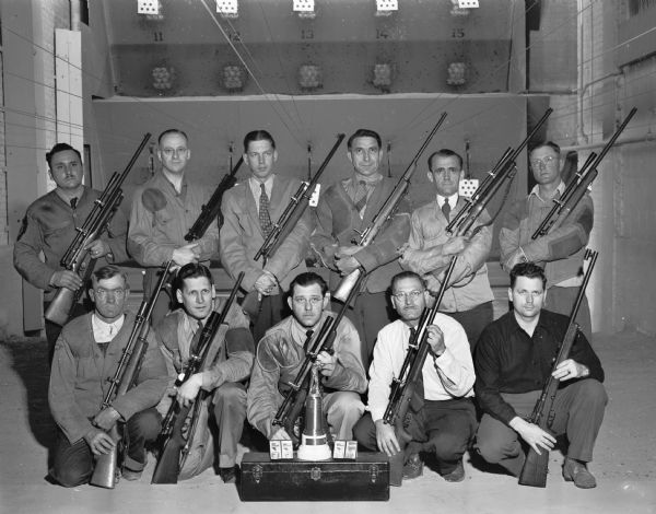 Eleven members of the Madison Rifle Club posed with rifles in a rifle range. They were Southern Wisconsin Rifle League Champions and a trophy with four medals is shown in the foreground.