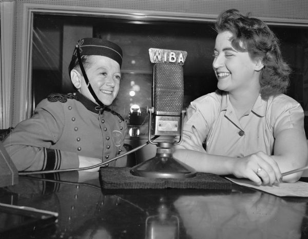 Johnny Roventini (known as "Johnny"), spokesman for Philip Morris cigarettes, is shown being interviewed by a woman at the WIBA radio station.