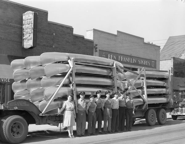 Al and Neva Reque and six of their salesmen standing in front of a load of new aluminum canoes, from Long Island, New York, at Madison Marine Service, 2102 Atwood Avenue.