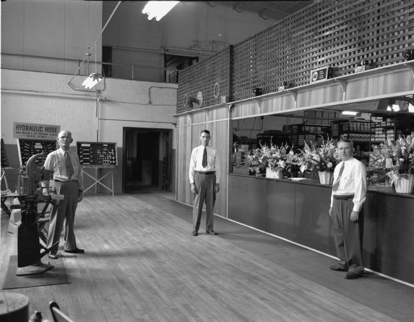 Interior view of Madison Armature Parts Company. Three men are standing in front of the counter with displays of flowers (opening day). The men are (?): James Gwin, President; Clarence M. Gwin, Vice President; and Dell Houser, Secretary-Treasurer.