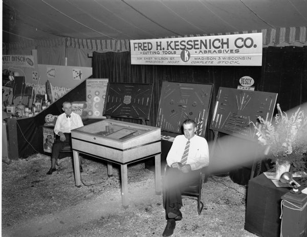 Two men sitting with the Fred H. Kessenich Co. (dealer in cutting tools and abrasives) booth at the East Side Business Men's Festival.