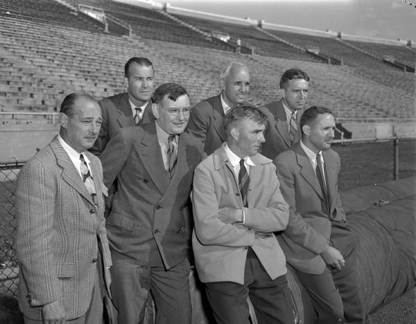 Seven high school coaches at the first North-South High School All-Star football game at Camp Randall. Back row, left to right: Ade Dillon, Appleton; Willis Jones, Madison East; Harold "Gus" Pollock, Madison Central. Front row, left to right: University of Wisconsin Athletic Director, Harold Stuhldreher; A.J. "Hunk" Barrett, Madison East; Lisle Blackbourn, Sr., Milwaukee Washington and Win Brockmeyer, Wausau.