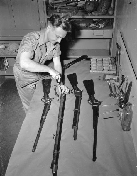Harold Peterson, a graduate assistant in history at the University of Wisconsin-Madison, shown working on some of the guns in the Wisconsin Historical Society's Collection. He later became a historian with the National Parks Service.
