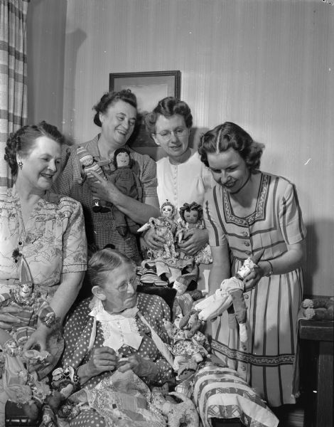 Women from the Unitarian Church with dolls for the war-blighted children of Europe and Asia. In the foreground is Mrs. F.H. (Ruby) King, one of Madison's oldest residents and one of the most loyal workers in the project.  Also shown are, left to right, Mrs. Ella Carter, president of the Womens' Society for Christmas Service of First Methodist Church; Mrs. Hans T. (Josephine) Sondergaard, Unitarian Church sewing committee; Mrs. Oscar L. (Tressie M.) Peterson, president of the Unitarian Womens' Alliance; Mrs. Alvin (Lillian L.) Breitzke, chairman of the Luther Memorial Church sewing group.