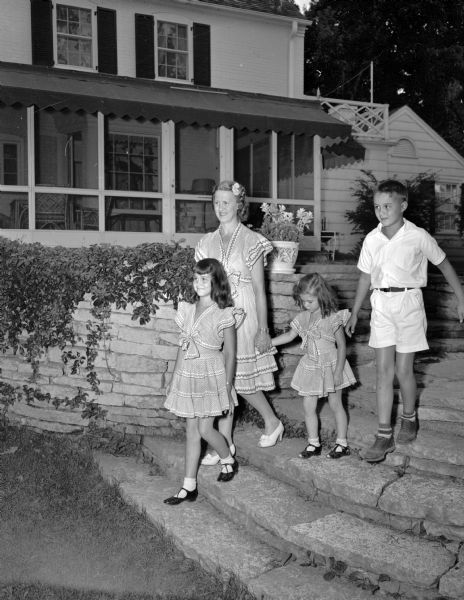 Mrs. Anthony R. (Dorothy) Curreri, 3636 Lake Mendota Drive, with her daughters Cynthia and Bonnie, and son Billy, walking on the flagstone steps of one of the terraces at their lakeside home. Mother and daughters are wearing identical blue and white printed frocks which Mrs. Curreri found in Mexico.