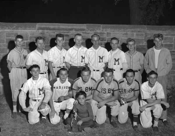 Group portrait of the East Side Business Men junior baseball team. A young boy is sitting in front holding a trophy.