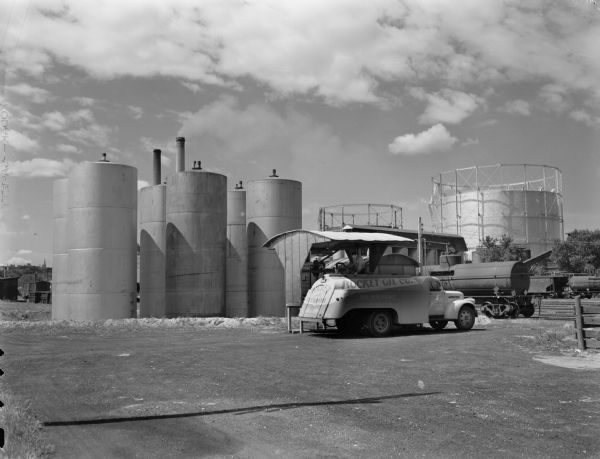 Rocket Oil Company fuel storage tanks at the bulk plant at 204 South Paterson Street.  In the foreground is a man on a modern Rocket Oil company truck filling it with lighter grade fuel oil which is used to heat homes.
