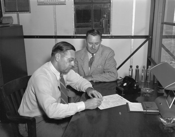 Man (probably R.O. Champeau, owner and operator of the Rocket Oil Company, 204 South Paterson Street), writing up an order for a customer who is seated to his left.