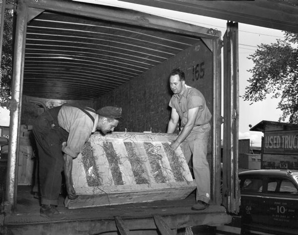 Two employees of the Bob Cooper Glass Company, 755 East Washington Avenue, unloading a crate of glass from a company truck at an undisclosed location.