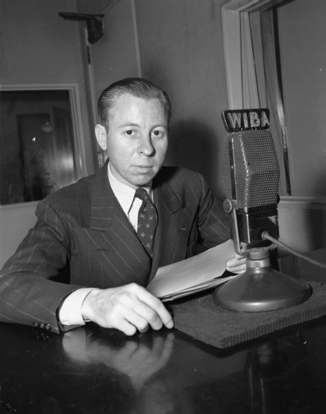 WIBA Program Director, Frank M. Bignell, seated behind a radio microphone.