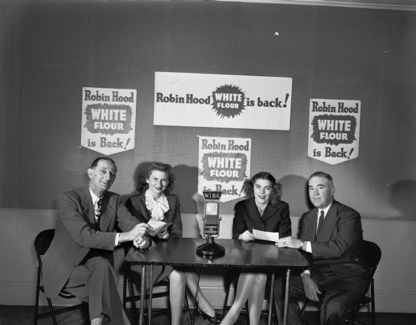 WIBA prize winners. Two couples seated behind a WIBA microphone with four Robin Hood White Flour posters on the wall.