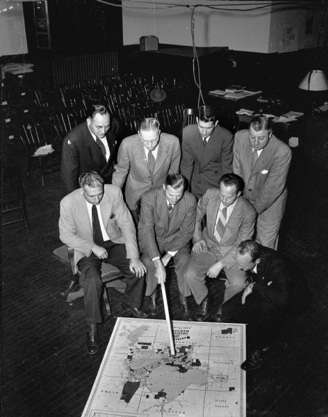 Madison men in charge of Community Chest campaign for small business firms looking at a city map. Sitting left to right: Leo Kronenberg, chairman of the East side; Charles Ellis, chairman of the Capitol Square; Fred M. Rentschler, chairman West side; and Robert Carnes. Standing left to right: Peter Norge, Herman Poast, Kenneth Rubadeaux, and Carl Regenberg, associate general chairman.