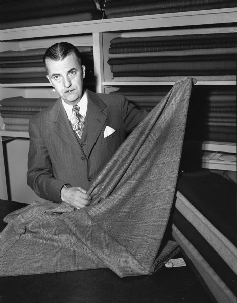 Herman Didricksen, tailor at Nedrebo Custom Clothing Company, 924 East Johnson Street, holding a bolt of cloth. Nedrebo's specializes in "garments expertly hand-cut and tailored to individual taste and measurement."