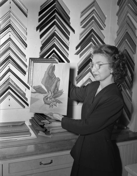 Frances Statz, daughter of Fred L. Statz, owner of the Fred. L. Statz Company, 123 West Main Street, shown displaying framed picture in front of display of picture frames.