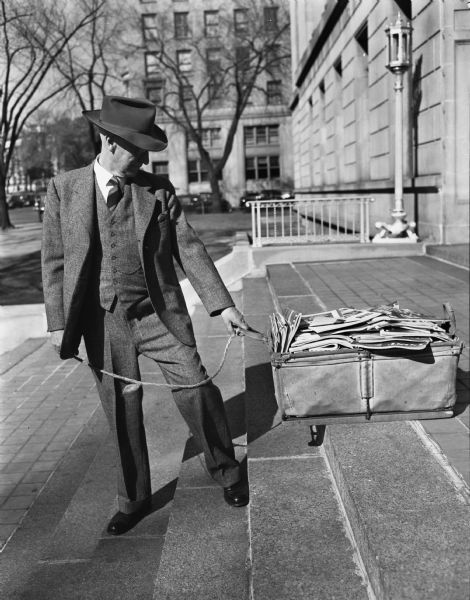 Clayton W. Haswell, 1610 Jefferson Street, on the steps of the United States Post Office Building, carefully guiding a wash basket filled with unclaimed magazines. Mr. Haswell distributes magazines to  Madison hospital patients as part of his membership in the Sunshine Committee of the Madison Kiwanis Club.