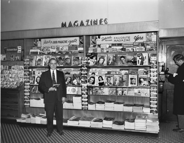 Edward C. Crossman, agency supervisor for Curtis Circulation Company, standing in front of a magazine rack at a Rennebohms Drugstore.
