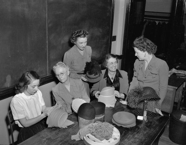 Five women members of the millinery class at Madison Vocational School admiring their finished hats. Left to right: Mrs. A.J. (Cora) Niebauer, Mrs. W. H.(Gladys) Konard, Mrs. Leo (Irene) Blied, Mrs. Ernest H. (Lorraine) Miller, and Mrs. George (Cordelia) Schultz.