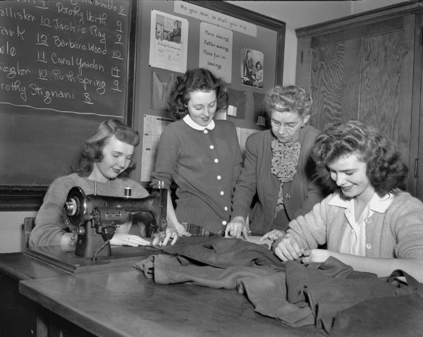 East High School clothing and homemaking teacher Helen Mathias (second from right), helping three of her students to make wool jumpers for the Junior Red Cross. The students are (left to right) Shirley Ann Ballam, Beverly Gilbert, and Ruth Kerwin.