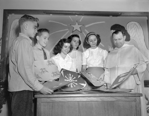 Blessed Sacrament School students (left to right), Jerry Quinn, Bill Laughnan, Mary Ann Petranek, Donna Wartner, and Maxine Watson, shown with hospital tray covers made for the Junior Red Cross.  Also shown is Reverend John B. Schneider.