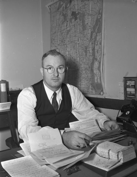 Portrait of a staff member of the Wisconsin Medical Society, 110 East Main Street (Tenney Building), seated at his desk working on papers.