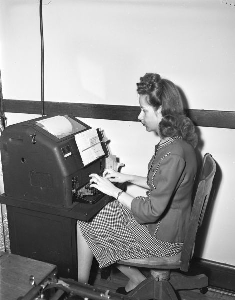 Portrait of woman employee of the Wisconsin Medical Society, 110 East Main Street, (Tenney Building) seated at teletype machine.
