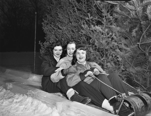 Winter scene with three girls seated on a toboggan. Left to right: Sue Ely, daughter of Arch and Marie, 4147 Iroquois Drive; Miriam Eye, daughter of Glen G. Eye, 1812 Kendall Avenue, and Janice Bondi, daughter of Hobart and Irene Bondi, 2019 Sherman Avenue.
