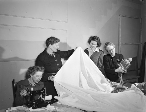 Group portrait of Madison Theater Guild members working on costumes for their production of "Alice in Wonderland". Left to right: Carrie Rasmussen, 916 Conklin Place; Mrs. Leslie E. (Evangeline) Brown, 4226 Waban Hill; Pearl Tesch, 804 Jenifer Street, chairman of the costume committee, and Mrs. Fred (Beulah) Reeth, 820 East Washington Avenue.
