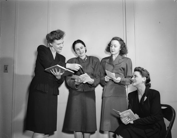 Group portrait of four women, members of the Madison Theater Guild, going over the script for their production of "Alice in Wonderland". Left to right: Nancy Eichsteadt, 139 Monroe Park, director;  Mrs. Bernard (Edna) Heilprin, Manitou Way, playing Tweedledee; Mrs. Jerome (Betty) Baer, 610 South Prospect Avenue, playing Tweedledum; and Mrs. Wade R. (Aleen) Plater, 403 Farwell Drive, cast as the Dormouse.