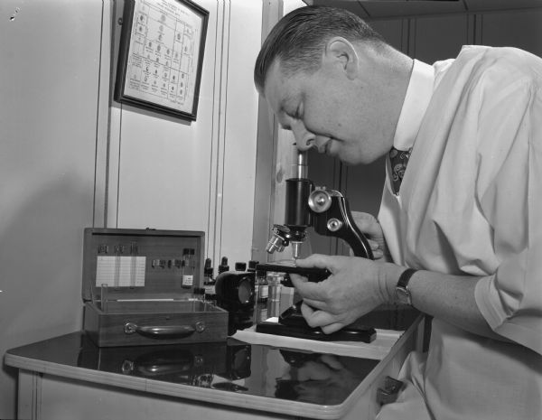 Dr. John H. Gieselman, osteopathic physician, shown at a microscope.  Dr. Gieselman often designed his own diagnostic equipment.  He invented a new mechanical microscope stage for systematic examination of microscopic slides.