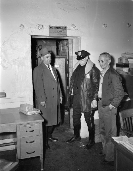 Drug salesman Harold Legler, Police Officer Howard Nelson, and clerk Al Hubin (left to right), are shown standing in the storeroom doorway at the Madison Drug Company, 654 Williamson Street, where they rescued the company manager from adhesive tape bindings placed on him by four armed bandits.