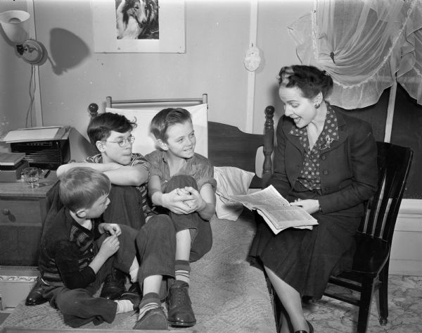 Margaret (Mrs. Norman) Vea reads to Ernest Underwood, of Theresa, Lloyd Riley, and Gerald Tilley, Brooklyn, at the Convalescent Home for Children with rheumatic fever. Margaret Vea is a member of the Zeta Phi Eta speech sorority.  The farmhouse of William and Frederike Weber on Highway 12-18, near the Yahara River south of Lake Monona, was the Children's Home for Rheumatic Fever cases ca. 1944-1947.