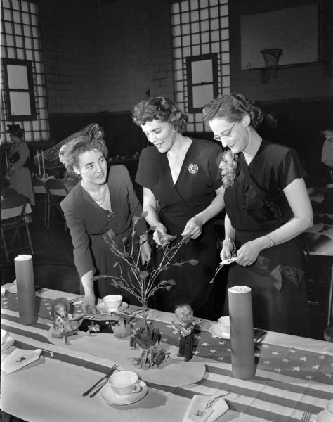 Three woman admire table decorations at the dessert bridge party of the Shorewood Hills Community League party.  Pictured from the left are: Mrs. James L. (Ruth) Noyes; Mrs. Harris G. (Marian) Allen; and Mrs. William (Jessie) Morgan.